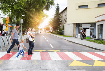 Young family with two boys in the city walking on a crosswalk - obrazy, fototapety, plakaty