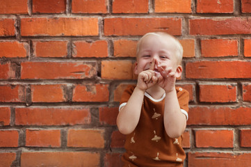 Cute little boy making funny faces on a brick wall background