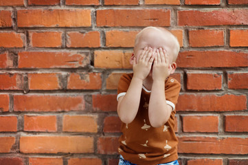 Cute little boy making funny faces on a brick wall background