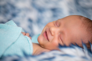 Śpiący mały chłopiec uśmiecha się podczas sesji noworodkowej.