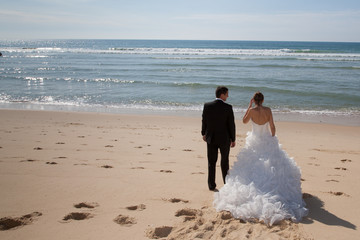 A rear view of a beautiful couple on the beach in wedding dress