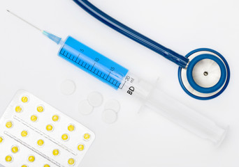 Stethoscope, pills and a syringe with blue liquid inside