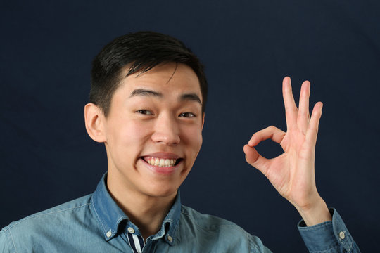 Smiling young Asian man giving okay sign
