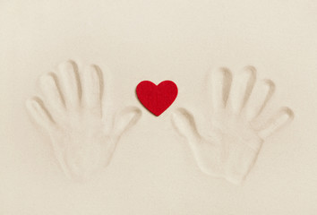 Zwei Hände im Sand halten ein rotes Herz