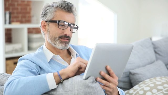 Mature man with eyeglasses websurfing on tablet at home