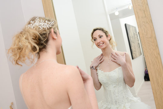 Beautiful young woman bride adjusting wedding dress in mirror