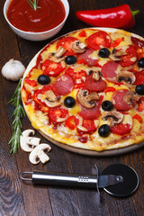 Pizza on wooden table with ingredients and cutter