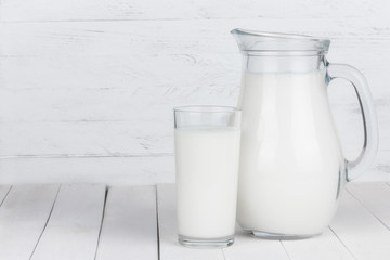 Glass of organic milk and full jar on white wooden table