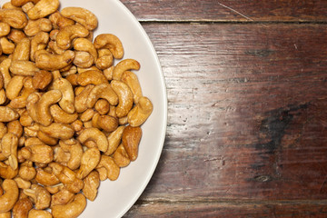Cashew nuts in white bowl on brown wooden table, top view.