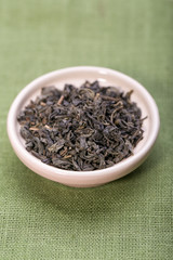 Bowl of dried green tea leaves on wooden background