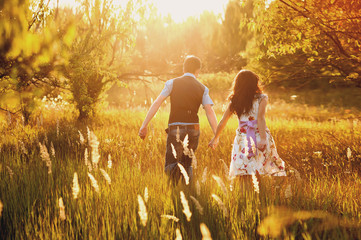 Fashionable cool couple runs across the field in sunset light
