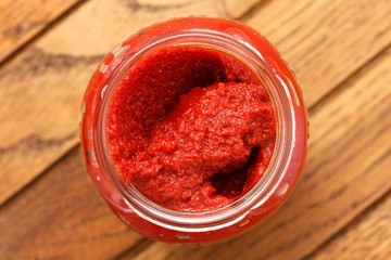 Open glass jar of tomato paste. On rustic wood surface.