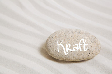 Wort Kraft auf einem Stein auf Sand als Hintergrund
