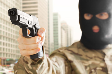 Man in black mask holding gun with city on background