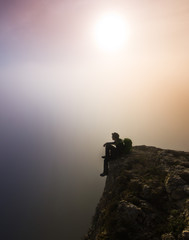 man sitting on a cliff in foggy weather