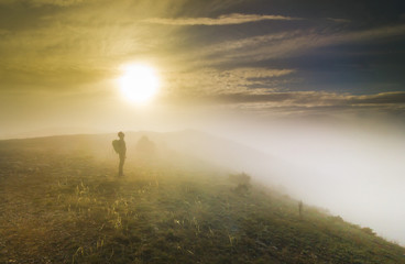 man standing on a hill in foggy weather at sunset