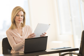 Businesswoman With Laptop Holding Resume In Office