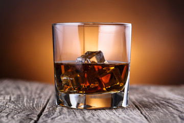 Glass of whiskey and ice on a wooden table.