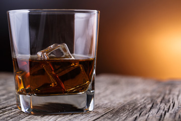 Glass of whiskey and ice on a wooden table.