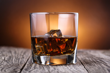 Glass of whiskey and ice on a wooden table.