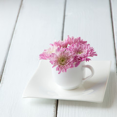 Cup full of pink  mum flowers on  old wooden table.