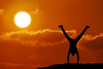 Silhouette of man on the mountain on sunset. Man stands on hands