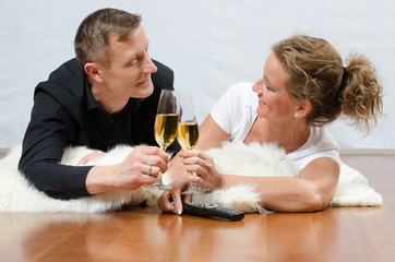 Paar liegt auf dem Boden und stösst mit Sekt an.