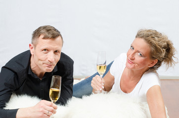 Paar liegt auf dem Boden und stösst mit Sekt an.