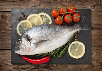 Fresh fish, lemon, spices and cherry tomatoes on a stone board