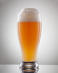Glass full of beer and foam on a gray background