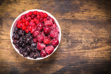 frozen berries in plate on wooden background