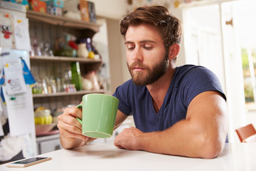Fototapeta na wymiar Young Man Sitting At Kitchen Table Drinking Coffee