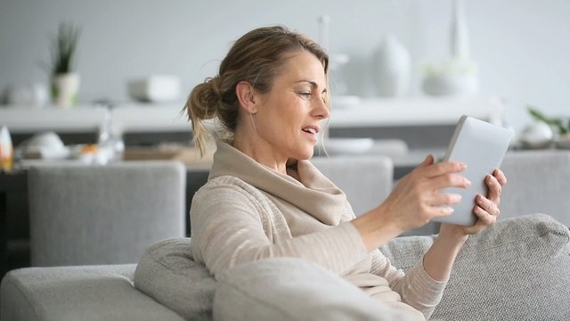 Mature woman sitting in sofa and websurfing on digital tablet