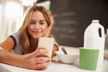 Young Woman Eating Breakfast Whilst Using Mobile Phone