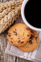 Cup of coffee with cookies and wheat on a wooden table.