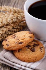 Cup of coffee with cookies and wheat on a wooden table.