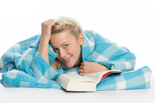 Blonde Frau liegt im Bett und liest ein Buch