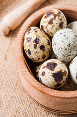 raw quail eggs in a wooden bowl on burlap background