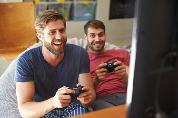 Two Male Friends In Pajamas Playing Video Game Together