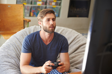 Man Wearing Pajamas Sitting In Chair And Playing Video Game © Monkey Business
