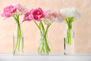 Fototapeta na wymiar Beautiful tulips in glass vases on light color background