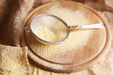 Flour with sieve on wooden cutting board, closeup