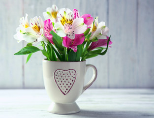 Beautiful flowers in cup, on wooden background