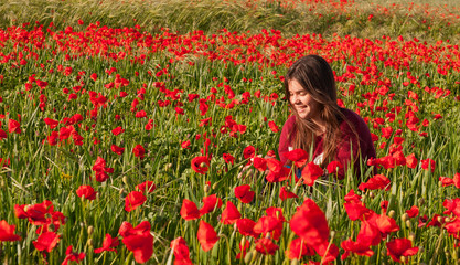 Happy smiling teenage girl sitting in a red poppy field