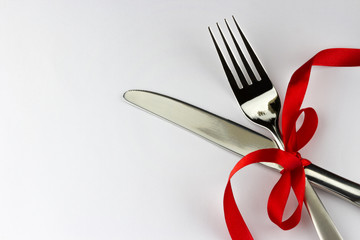 Top view of silver fork and knife decorated red ribbon with bow 