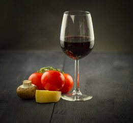 Vegetables and glass of vine on dark wooden background