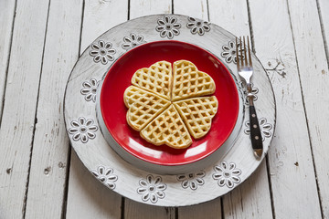 Selbstgemachte Herzwaffeln,roter Teller, weißer Holztisch