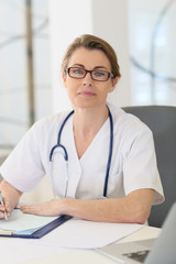 Portrait of mature nurse sitting at desk in office