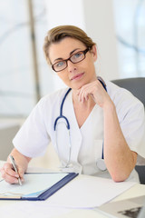 Portrait of mature nurse sitting at desk in office