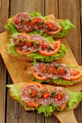 Sandwiches with ham, salad leaves, chili, tomatoes, capers, fren